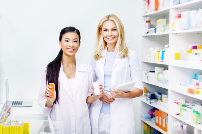 female pharmacists with digital tablet and medication smiling at camera in drugstore